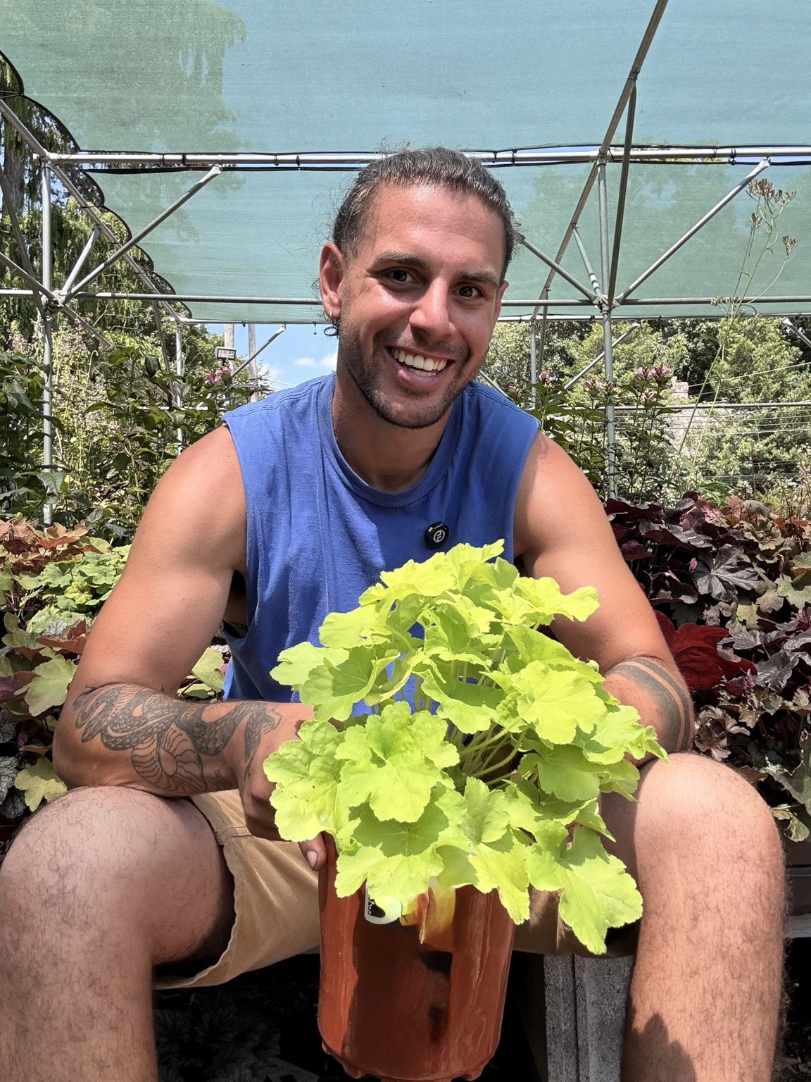 Jay smiling while holding a bright green foliage plant at the nursery